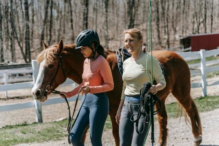 Two women walking with a horse in a serene outdoor setting, enjoying a sunny day.